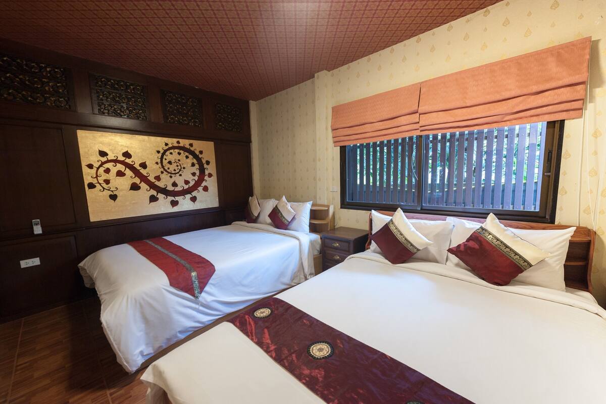 A hotel room with two beds, a decorative wall, a window with blinds, and a tiled ceiling.