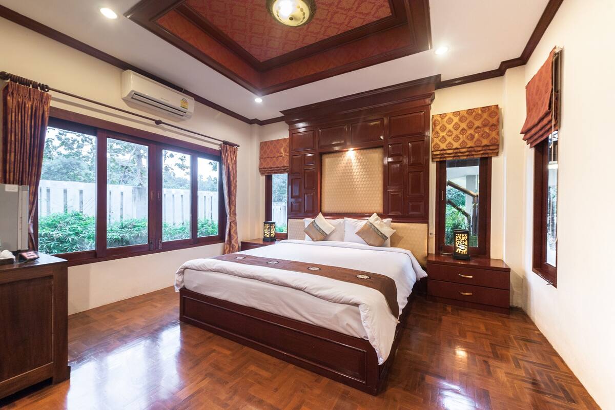 A spacious bedroom with a large bed, wooden furniture, and large windows.