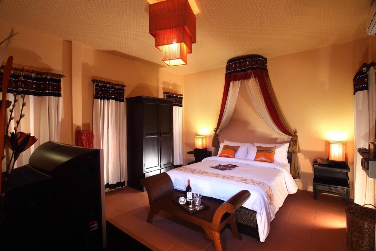 A hotel room with a bed, a TV, a table with a bottle and glasses, and a chair.