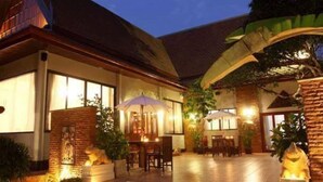 A well-lit, multi-level outdoor area with steps leading up to a patio, surrounded by potted plants and a dining area with umbrellas. - Ruen Ariya Resort (Mae Rim)