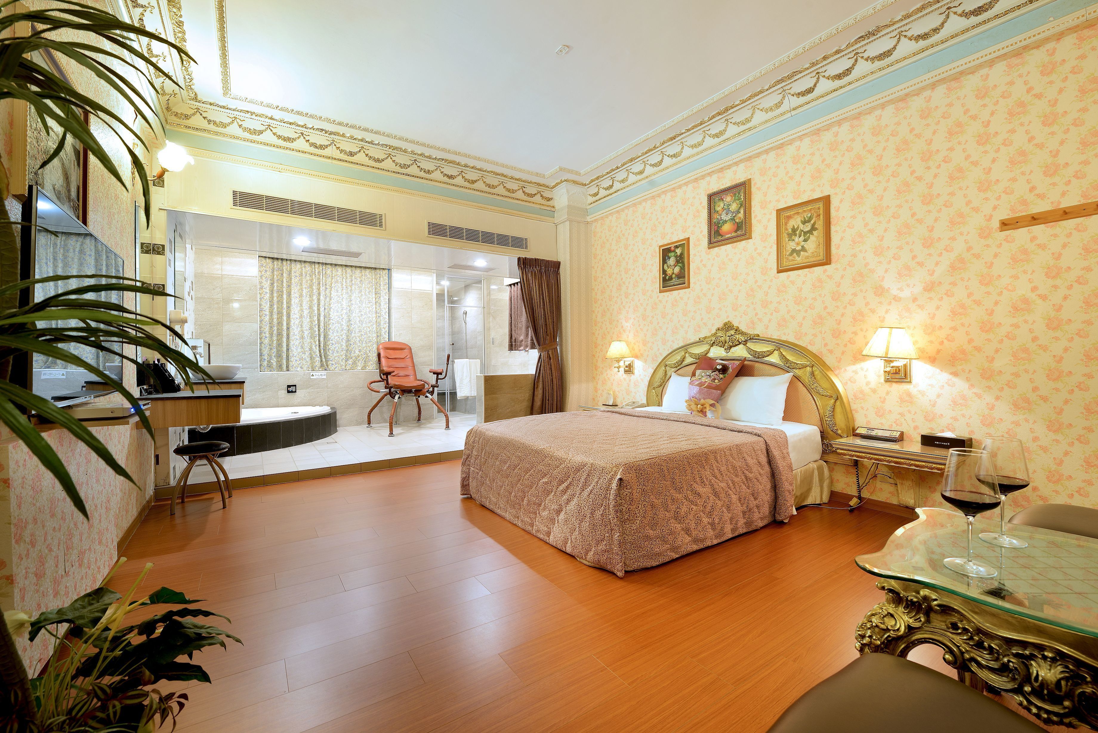 Une chambre d’hôtel comprenant un lit, un bureau, une chaise, une table en verre avec un verre à vin et une plante en pot.
