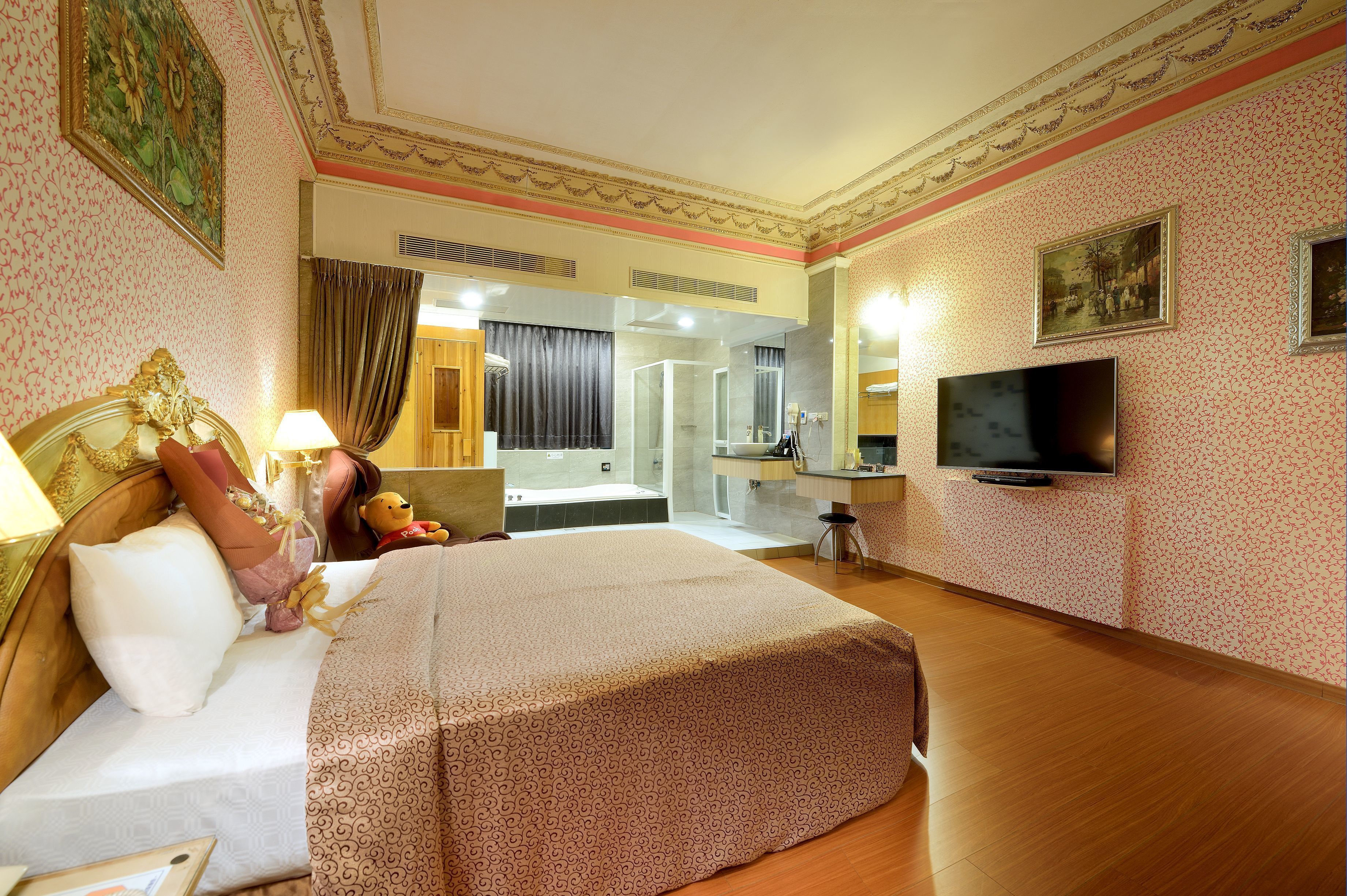 Habitación de hotel con una cama grande, televisión, escritorio con silla, espejo y baño visible a través de una puerta abierta.
