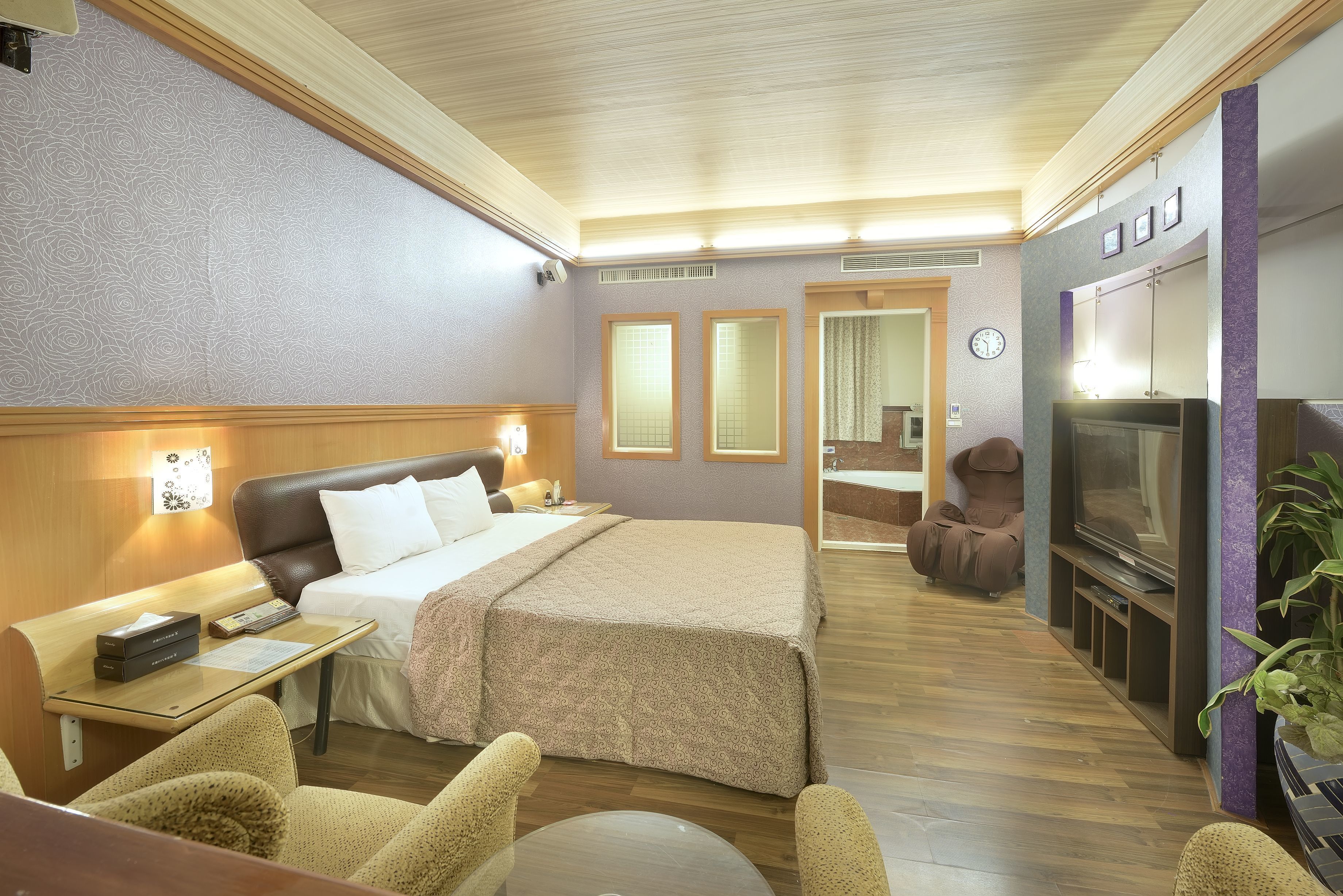 A hotel room with a bed, bedside table, lamp, TV, seating area, and a mirror.