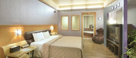 A hotel room with a bed, bedside table, lamp, TV, seating area, and a mirror.