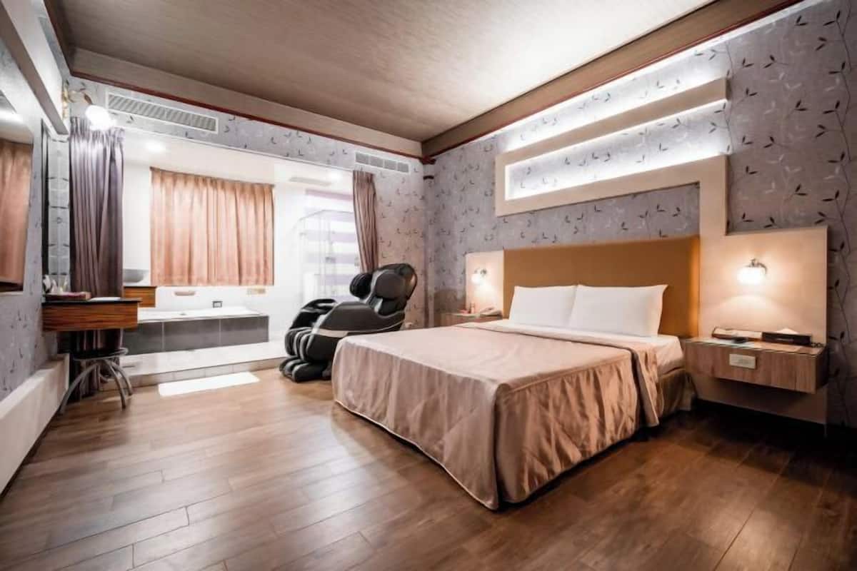 Una camera d'albergo con un letto, una poltrona massaggiante, una scrivania e una finestra con tende.