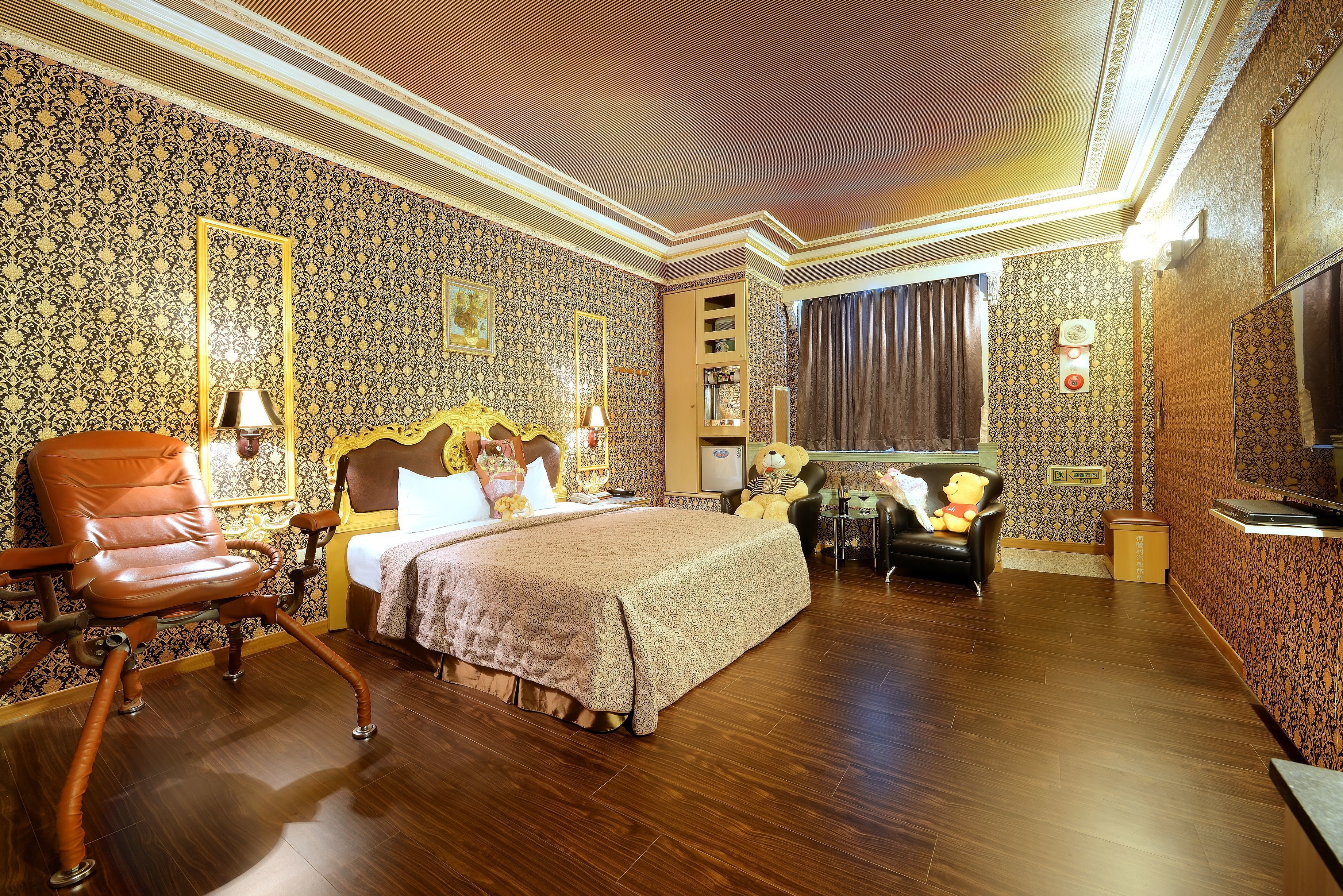 A hotel room with a large bed, a leather armchair, a desk with a chair, and a television.