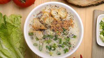 A bowl of soup with toppings, surrounded by vegetables and a wooden background.