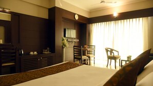 A hotel room with a bed, a desk, a chair, a small table, and a window with curtains. - Hotel Pearl International (Chennai)