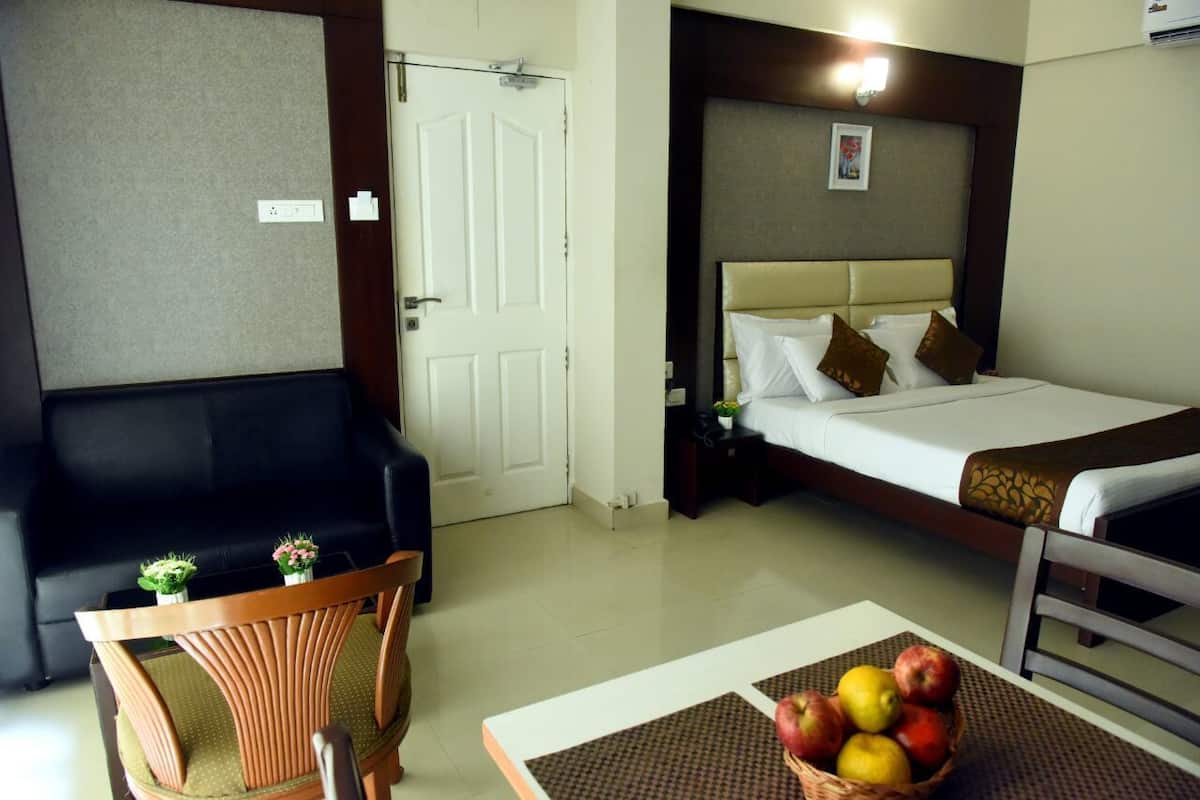 A hotel room with a bed, a small table with a fruit basket, a chair, and a sofa.