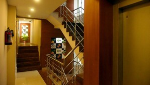 A staircase with metal railings leading to an upper floor, a fire extinguisher mounted on the wall, and a door with a window on the right. - Hotel Pearl International (Chennai)