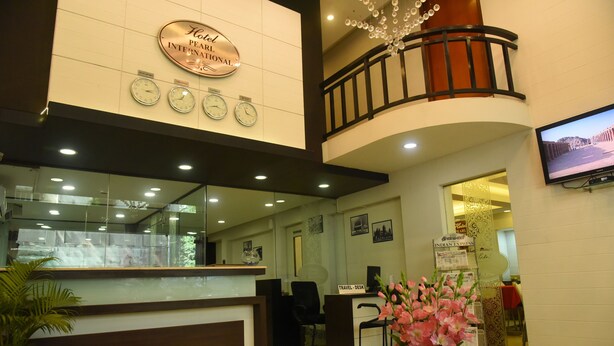 A hotel reception area with a clock, a travel desk, and a TV screen. - Hotel Pearl International (Chennai)