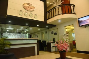 A hotel reception area with a clock, a travel desk, and a TV screen.