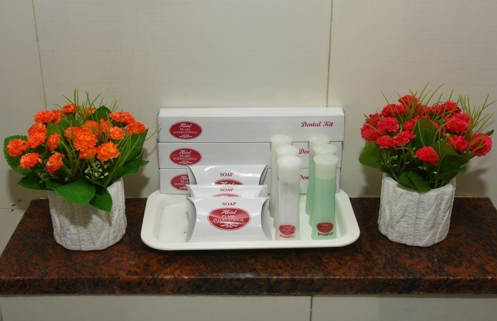 Una bandeja con artículos de aseo, incluyendo jabón y champú, ubicada entre dos arreglos florales sobre una encimera.
