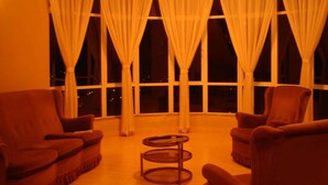 Una habitación con dos sillones, una mesita redonda y ventanas amplias con cortinas.