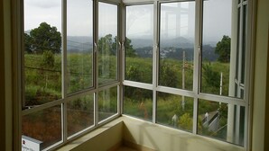 Habitación de esquina con un amplio ventanal que ofrece vistas a un paisaje verde y edificios al fondo.
