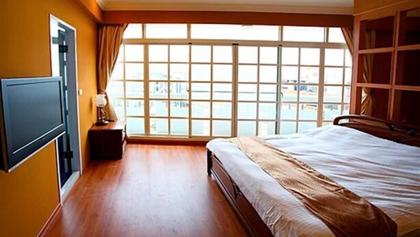 Una habitación de hotel con un ventanal grande, una cama, un televisor y una mesita de noche.