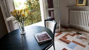 Une pièce avec une table ronde, un vase rempli de fleurs, un tableau encadré accroché au mur et un radiateur.