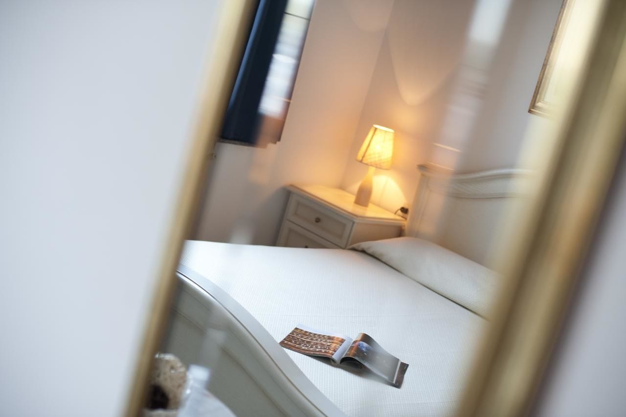 A hotel room with a bed, a nightstand, a lamp, and a magazine on the bed.