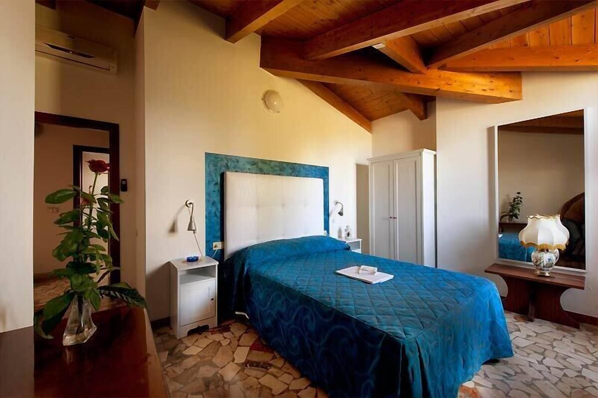 Un dormitorio con una cama grande, una mesita de noche, un espejo y una planta en maceta.