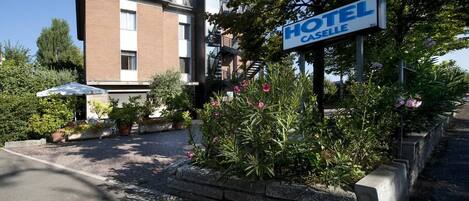 A hotel sign with "HOTEL CASSELLE" written on it, surrounded by greenery and a paved driveway.