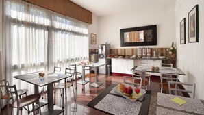 Une cuisine moderne avec des meubles blancs, un coin repas avec une table dressée pour deux personnes et une grande fenêtre ornée de rideaux légers.