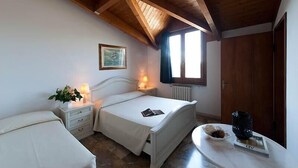 Une chambre avec deux lits, un plafond en bois, une fenêtre, un radiateur et une table de chevet avec une lampe et un livre.