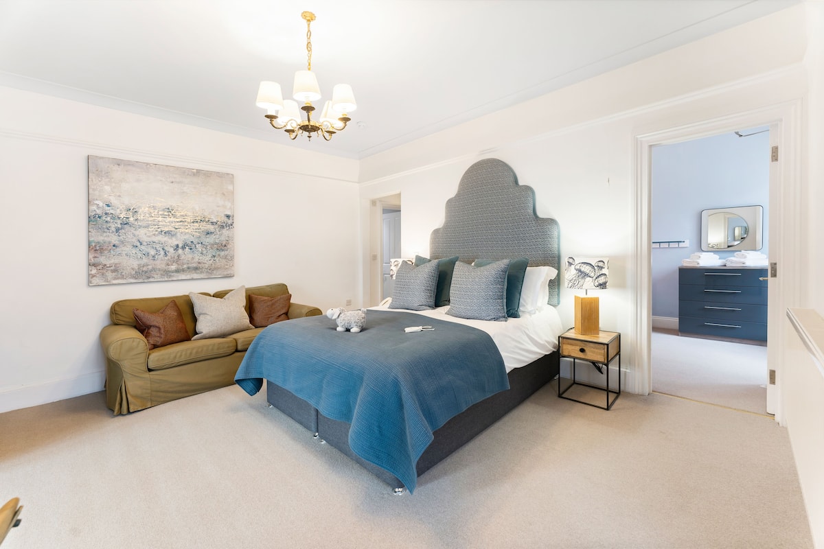A bedroom with a bed, a nightstand, a dresser, a sofa, and a painting on the wall.