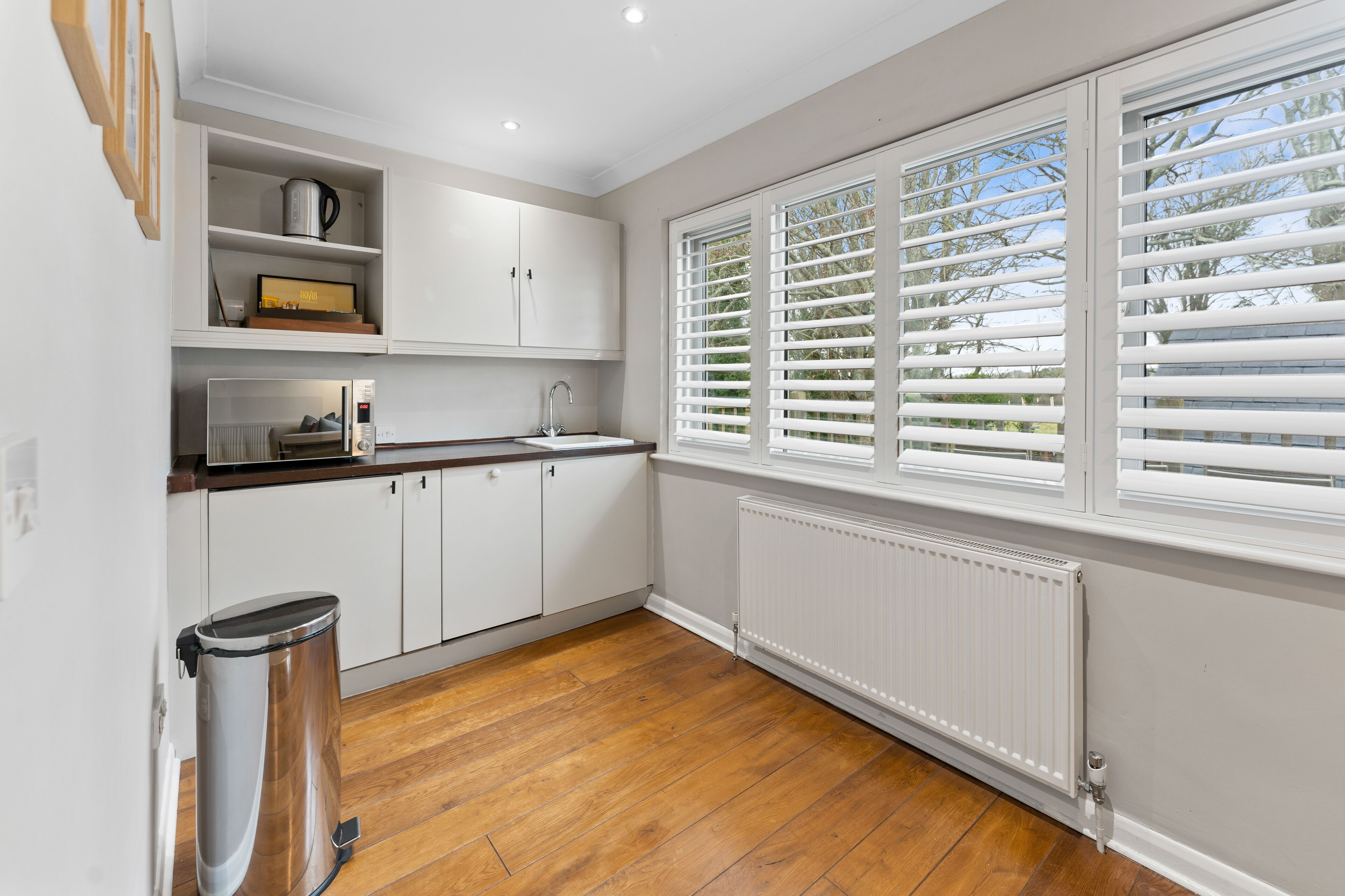 A kitchen with white cabinets, a wooden countertop, a window with blinds, and a radiator.