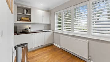 A kitchen with white cabinets, a wooden countertop, a window with blinds, and a radiator.