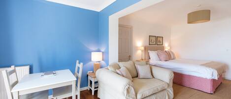 Un dormitorio con cama, mesita de noche, lámpara y silla.