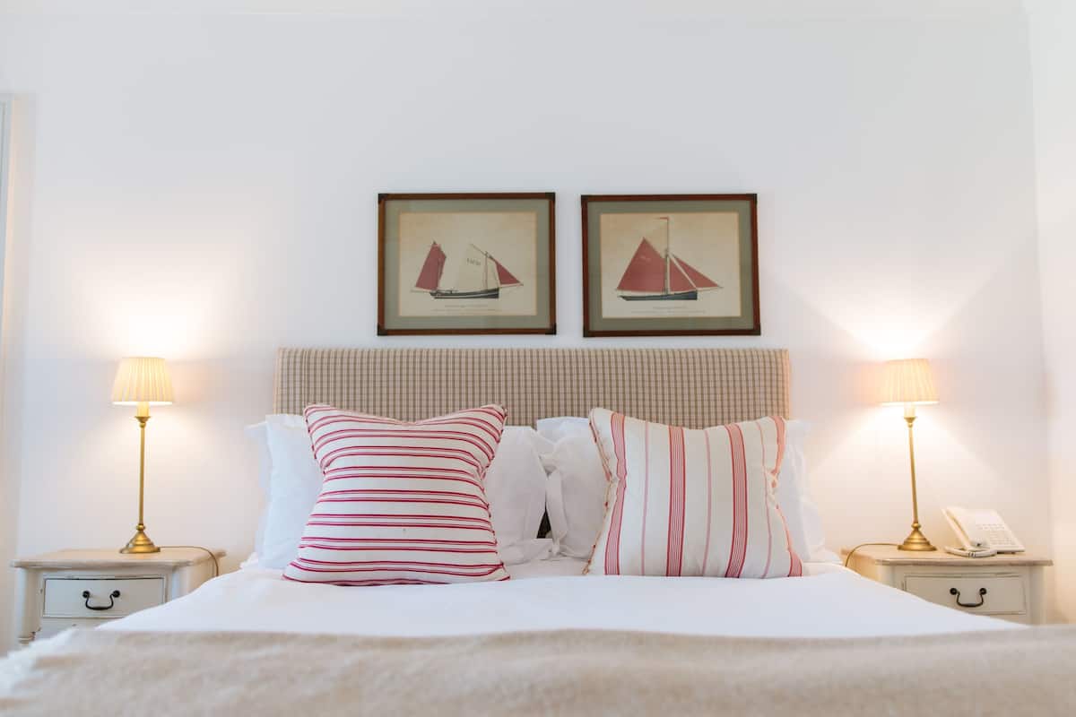 A neatly made bed with striped pillows, two framed sailboat pictures on the wall, and bedside lamps on nightstands.
