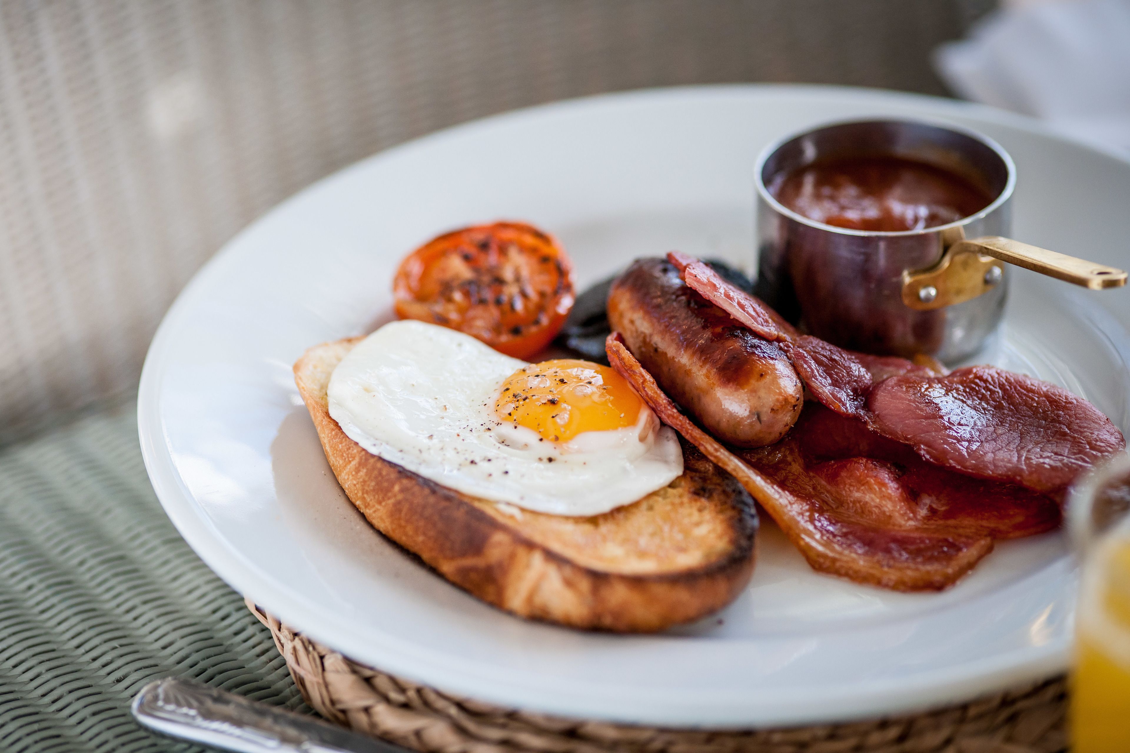 A plate with toast, a fried egg, bacon, and a tomato on a woven mat.