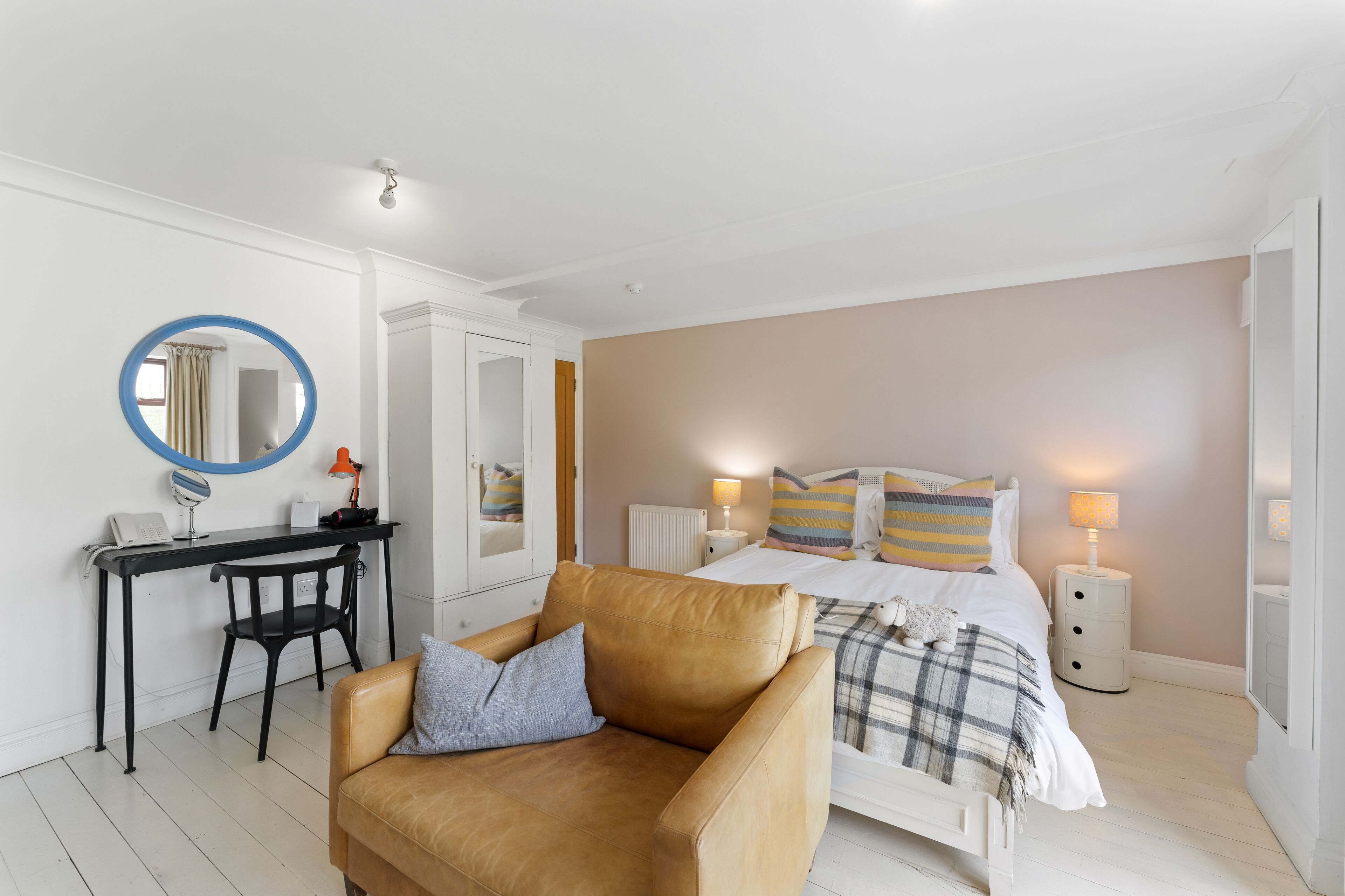 A bedroom with a bed, a desk, a chair, a round mirror, and bedside lamps.