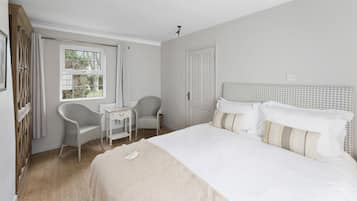 A bedroom with a large bed, a desk, two chairs, and a window.