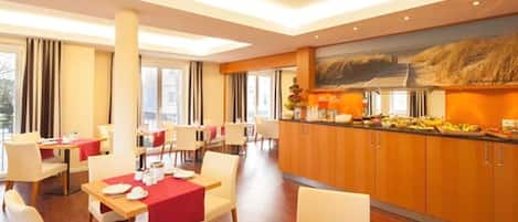 A modern dining area with tables set for breakfast, a buffet counter, and a large window providing a view of the city.