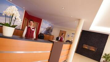 A reception area with a wooden reception desk, a large potted orchid, a fireplace, and a painting on the wall.
