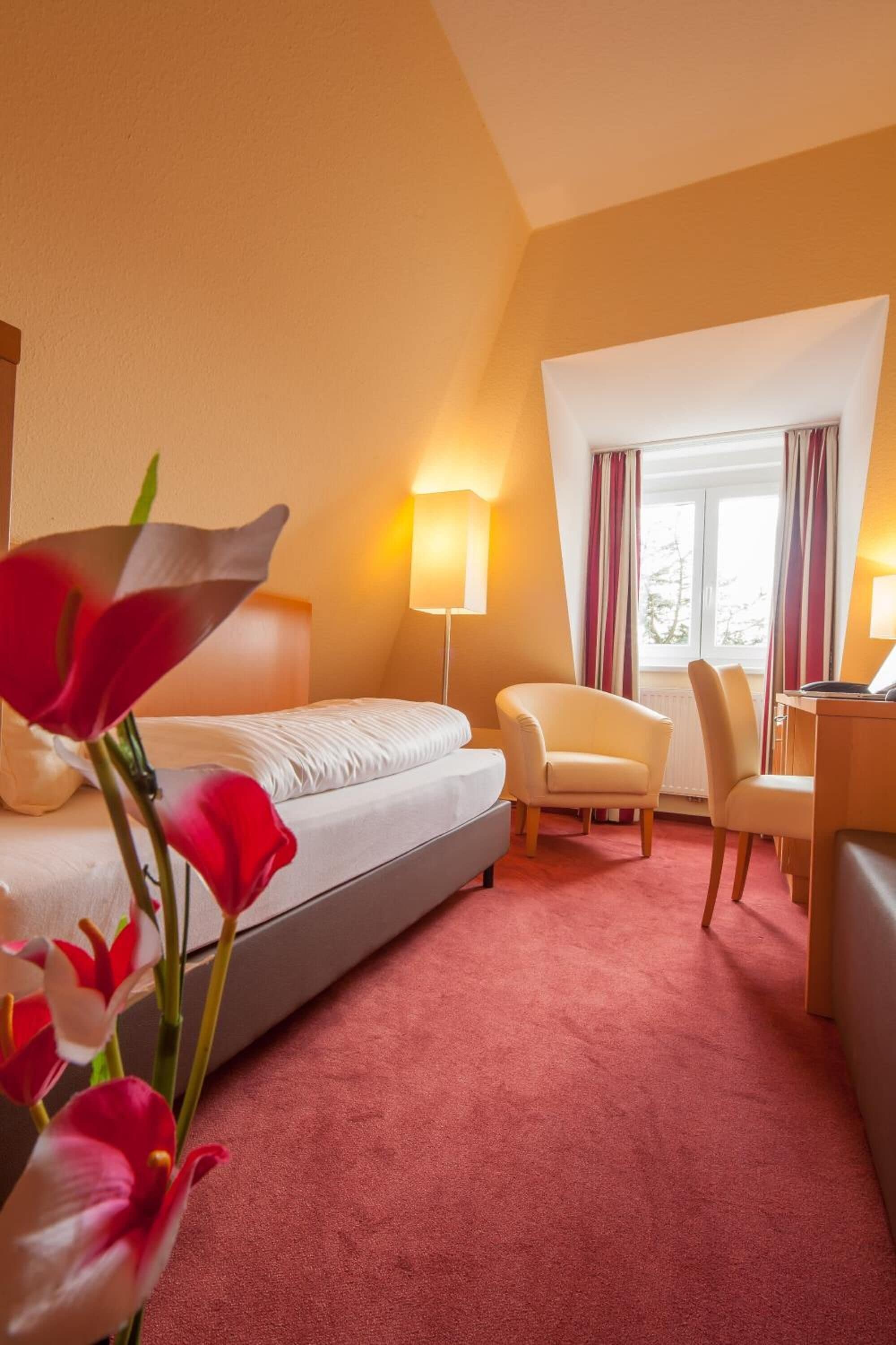 Una habitación de hotel con una cama, dos sillas, un escritorio, una lámpara y una ventana con cortinas.