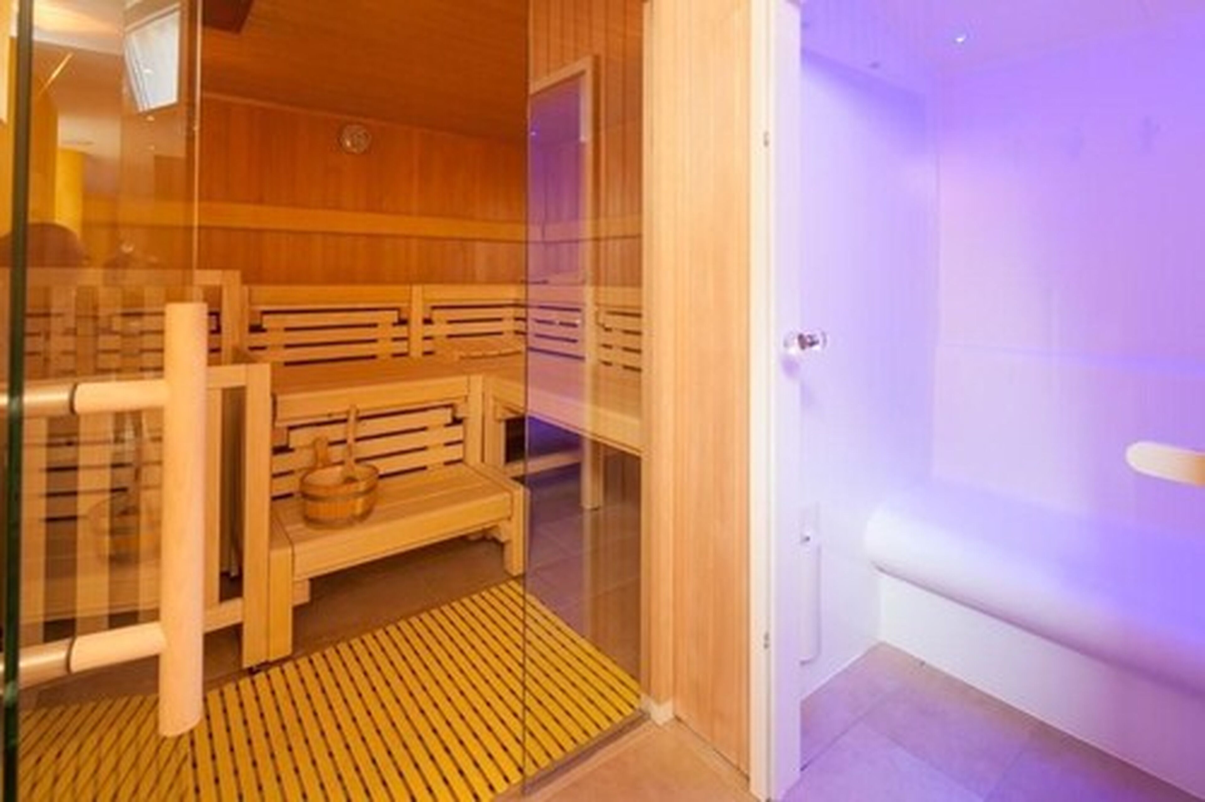 Un sauna avec des bancs en bois et une porte d’entrée en verre.