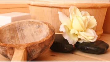 A wooden bowl, a white soap bar, and a flower on a wooden surface.