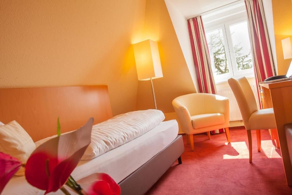 A hotel room with a bed, a desk, a chair, and a window with curtains.