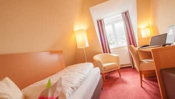 A hotel room with a bed, a desk with a laptop, a chair, and a window with curtains.