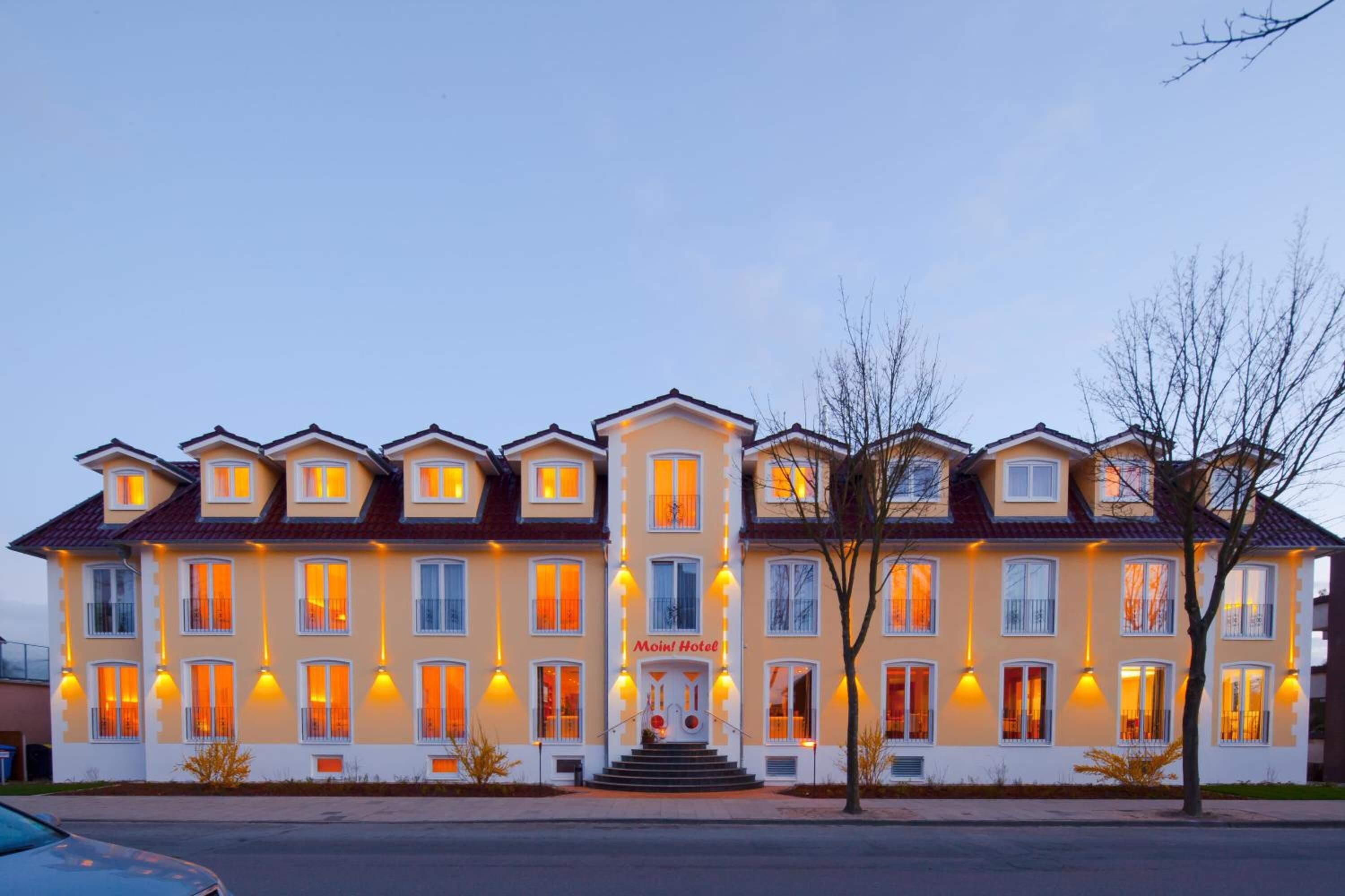 A multi-story hotel with a central entrance, balconies, and uniform lighting.