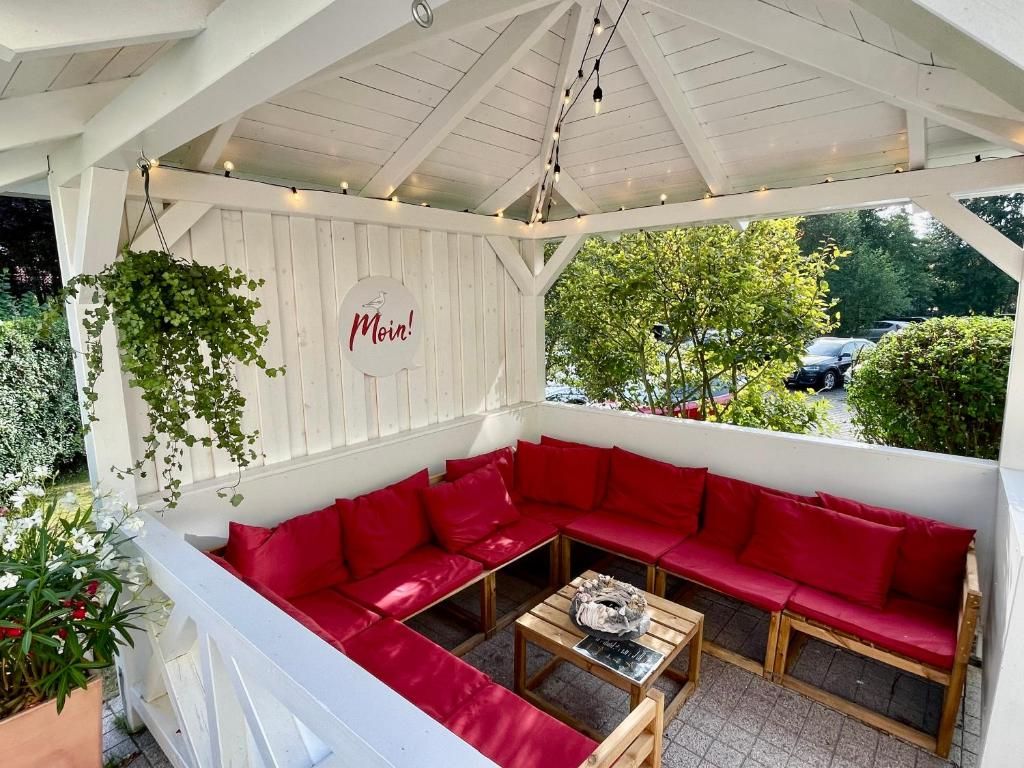 A covered outdoor seating area with red cushions and a wooden table.