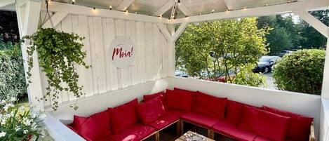 A covered outdoor seating area with red cushions and a wooden table.