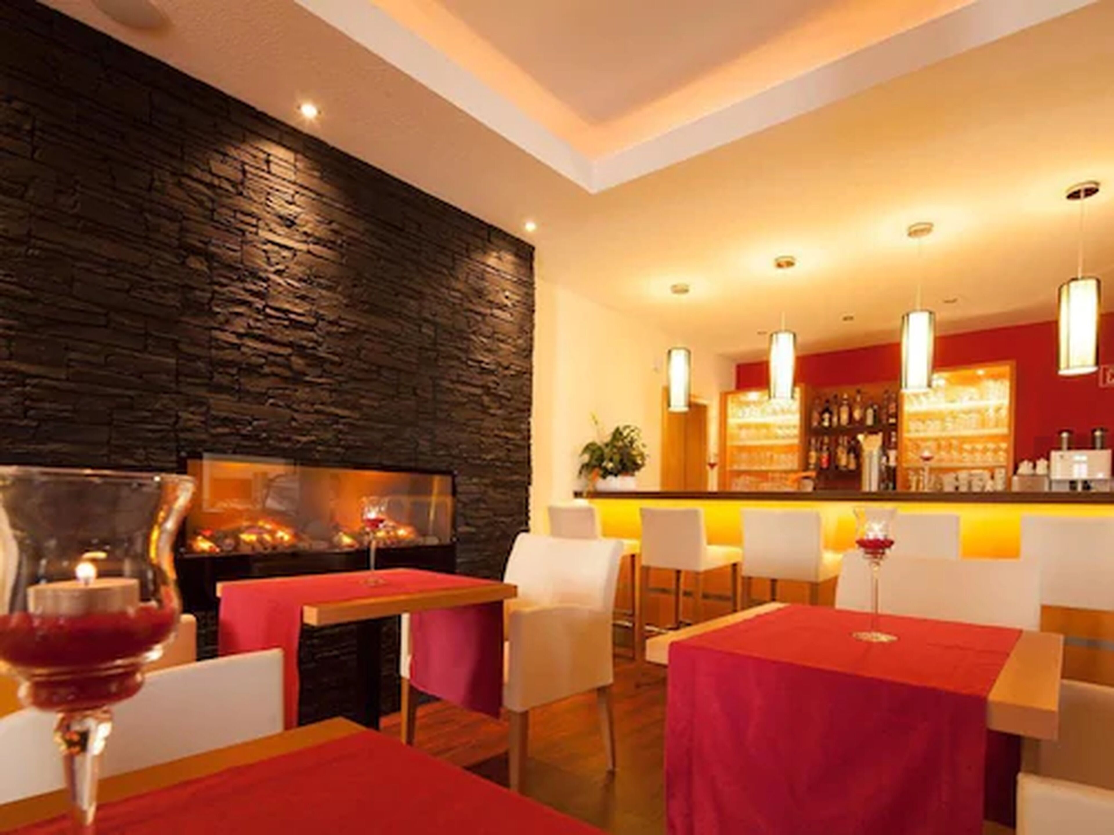 Un restaurant avec un mur en pierre, des tables rouges et des chaises blanches.