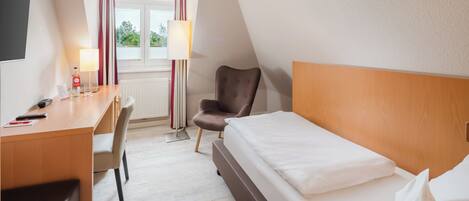 A hotel room with a bed, a desk, a chair, a lamp, and a window with curtains.