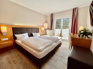 A hotel room with a double bed, bedside lamps, a desk, and a view of the outdoors.
