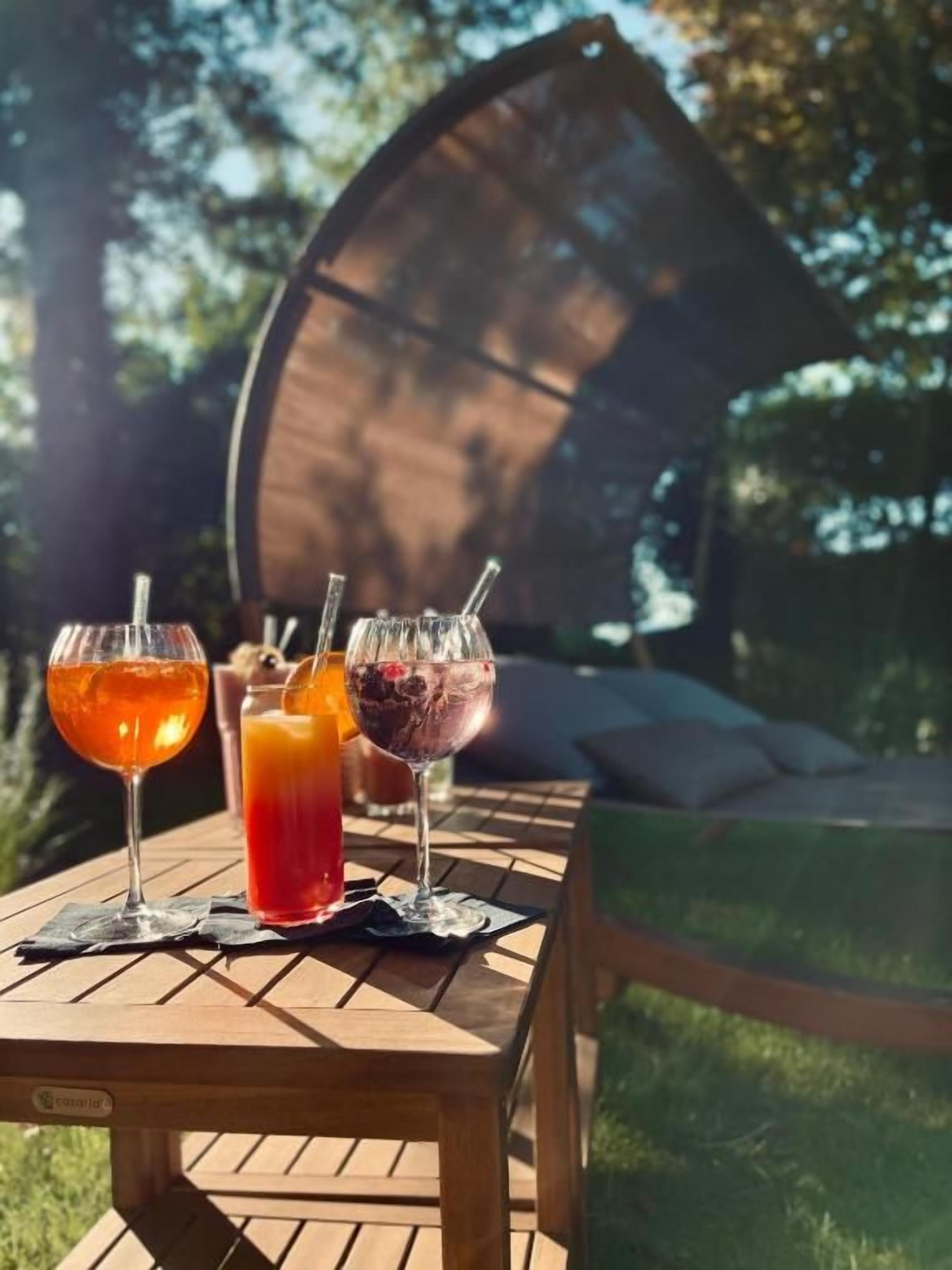 Une table en bois avec trois boissons, un banc et, au fond, un espace abrité.