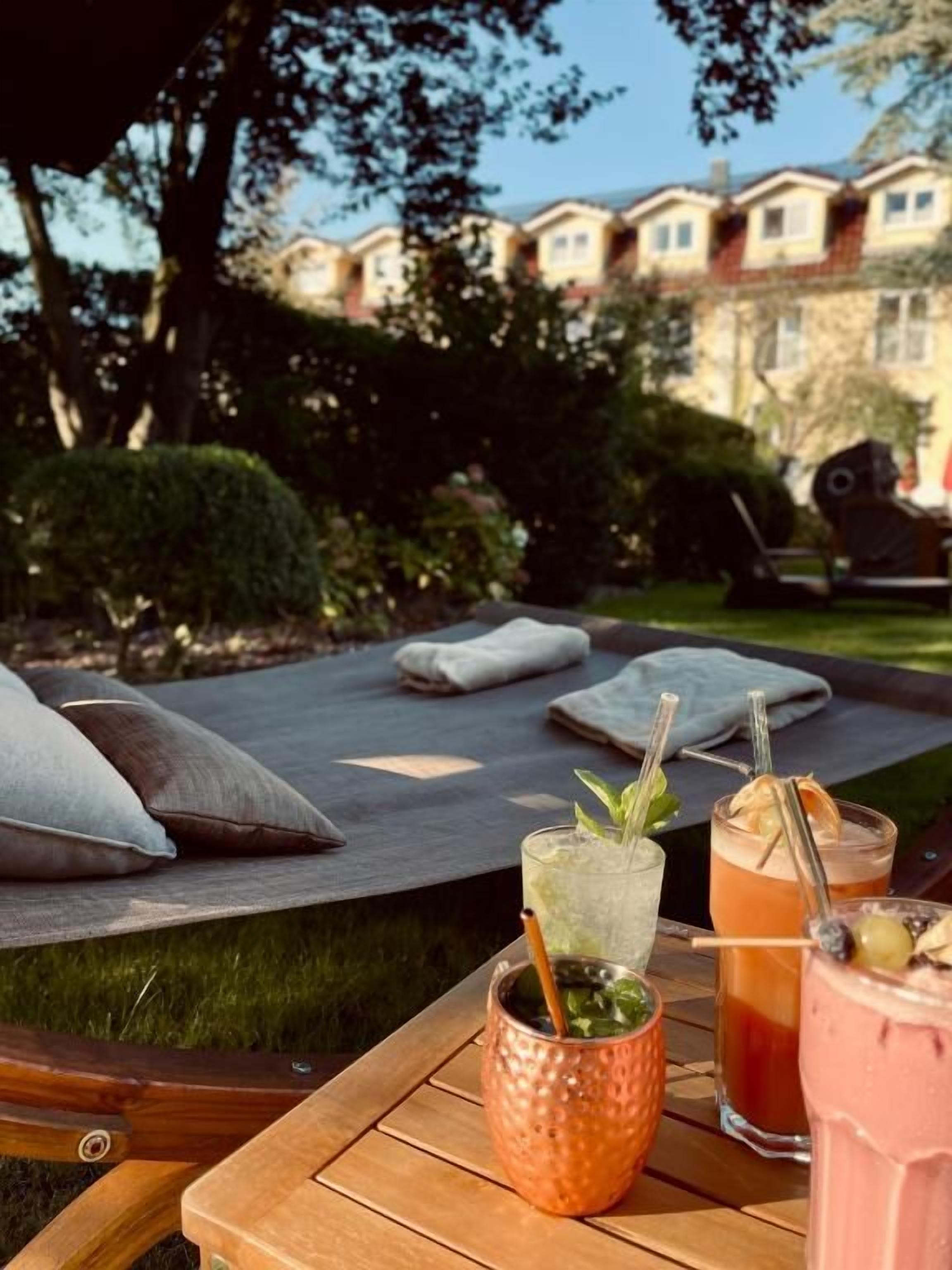 Una mesa de madera con bebidas y un cojín en un jardín.