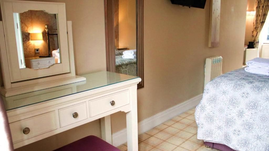 A bedroom with a glass-top dresser, a bed with patterned bedding, a mirror, and a radiator.